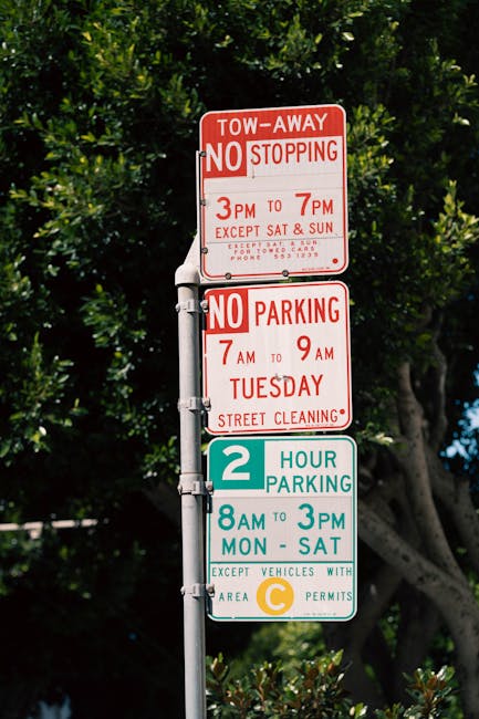 A metal street signpost with three rectangular signs attached, set against a backdrop of dense green foliage and partly cloudy sky. The top sign is red and white, indicating tow-away restrictions with no stopping from 3 pm to 7 pm, except on weekends, and provides a contact number for towered cars. The middle sign, also in red and white, states no parking from 7 am to 9 am on Tuesdays, designated for street cleaning. The bottom sign features a white background with green, blue, and yellow elements, indicating a two-hour parking limit from 8 am to 3 pm, Monday through Saturday, with an exception for vehicles displaying area C permits. The signs are mounted on a gray metal pole, which is secured with bolted brackets, and the overall scene suggests regulations for parking and roadside management in an urban or suburban area, with the presence of lush trees providing environmental context for the location. The signs are clearly visible with distinct colors and text, reflecting local parking rules and restrictions, possibly relevant to private or alternative waste management considerations for residents and service providers like rubbish clearance companies such as error code: 522.